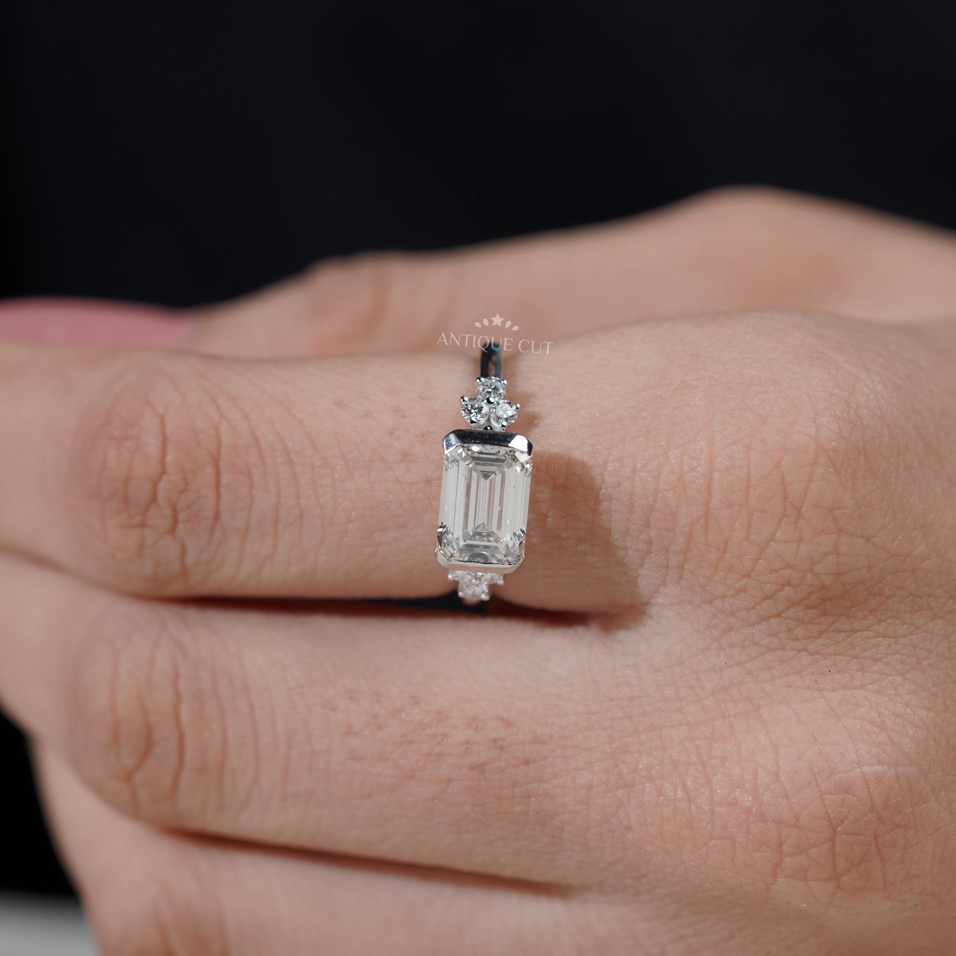 Diamond ring with emerald-cut center stone and smaller diamonds on a gradient background

