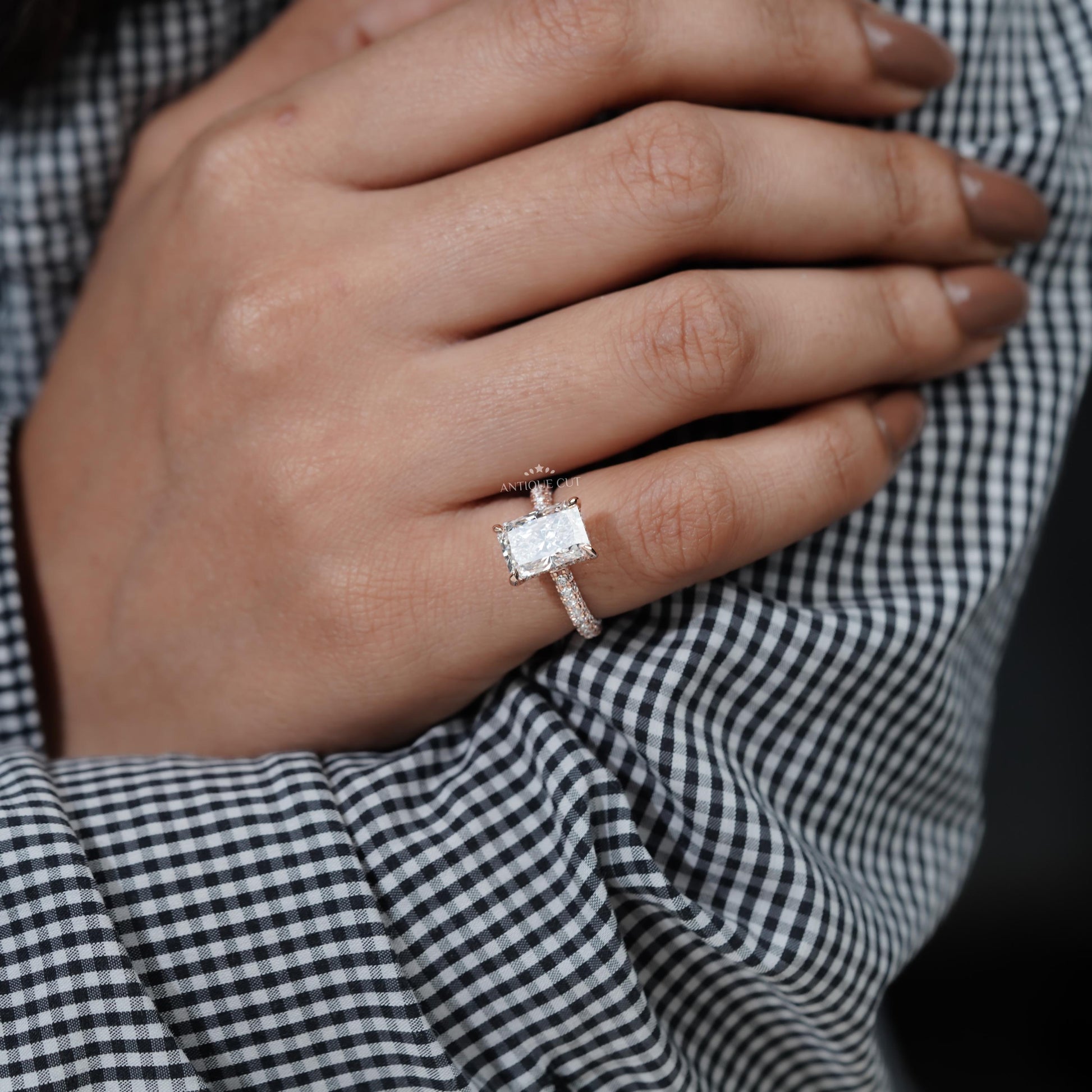 Hand wearing a diamond ring with a checkered fabric background

