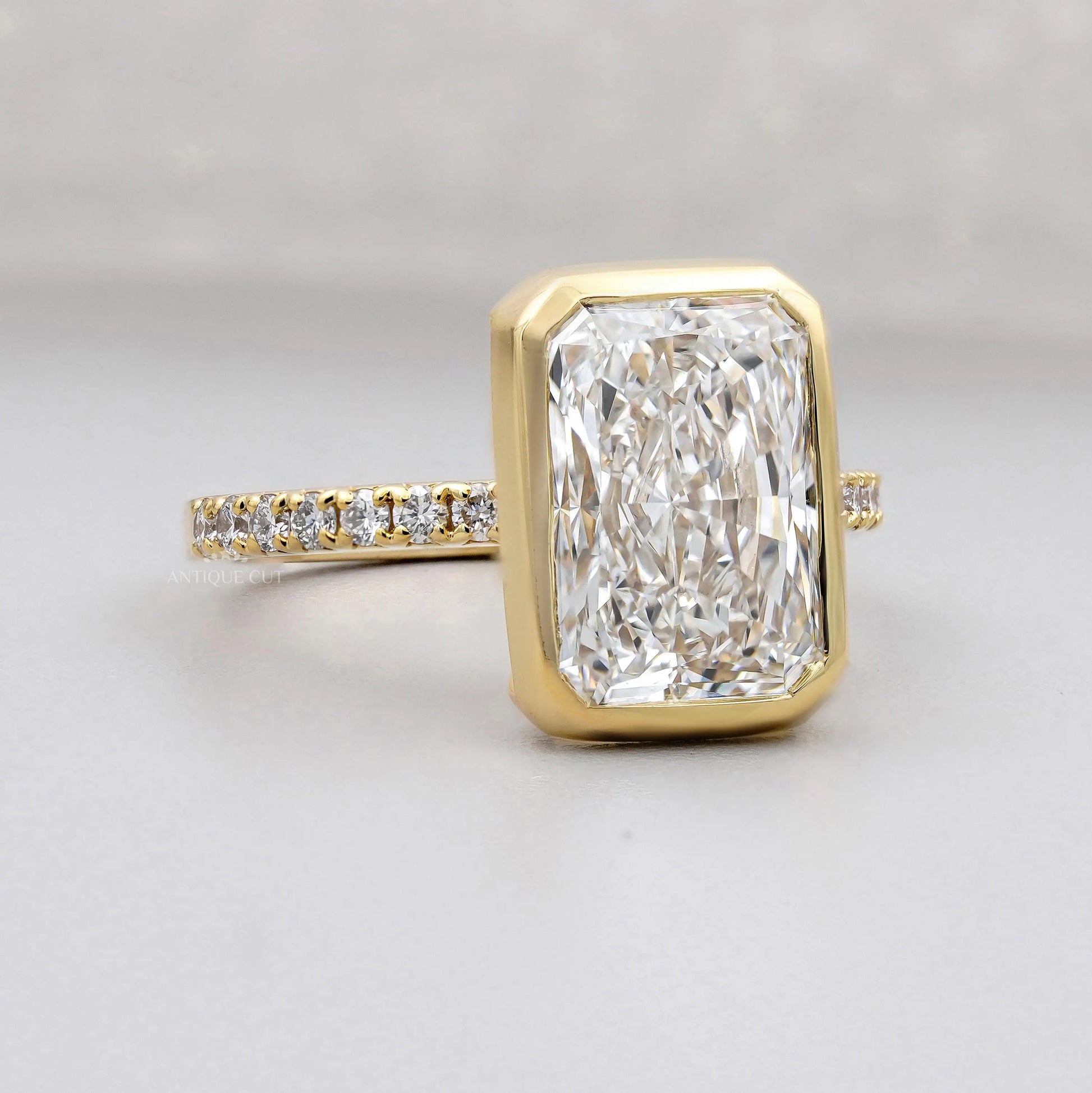 Gold ring with a large diamond and smaller diamonds on the band against a gray background