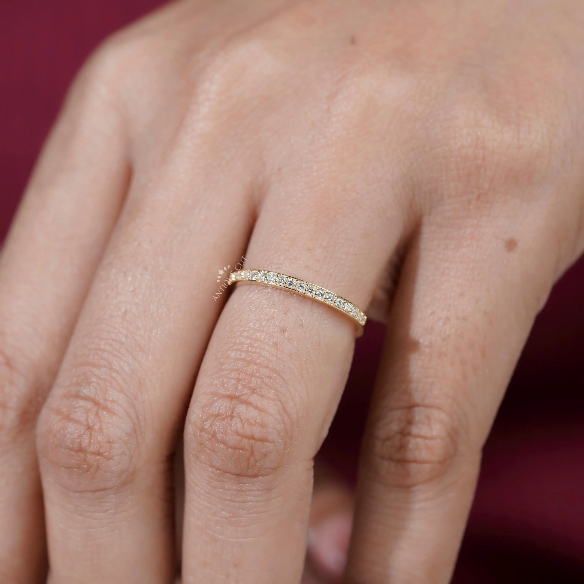Gold ring with small diamonds on a person's finger against a red background