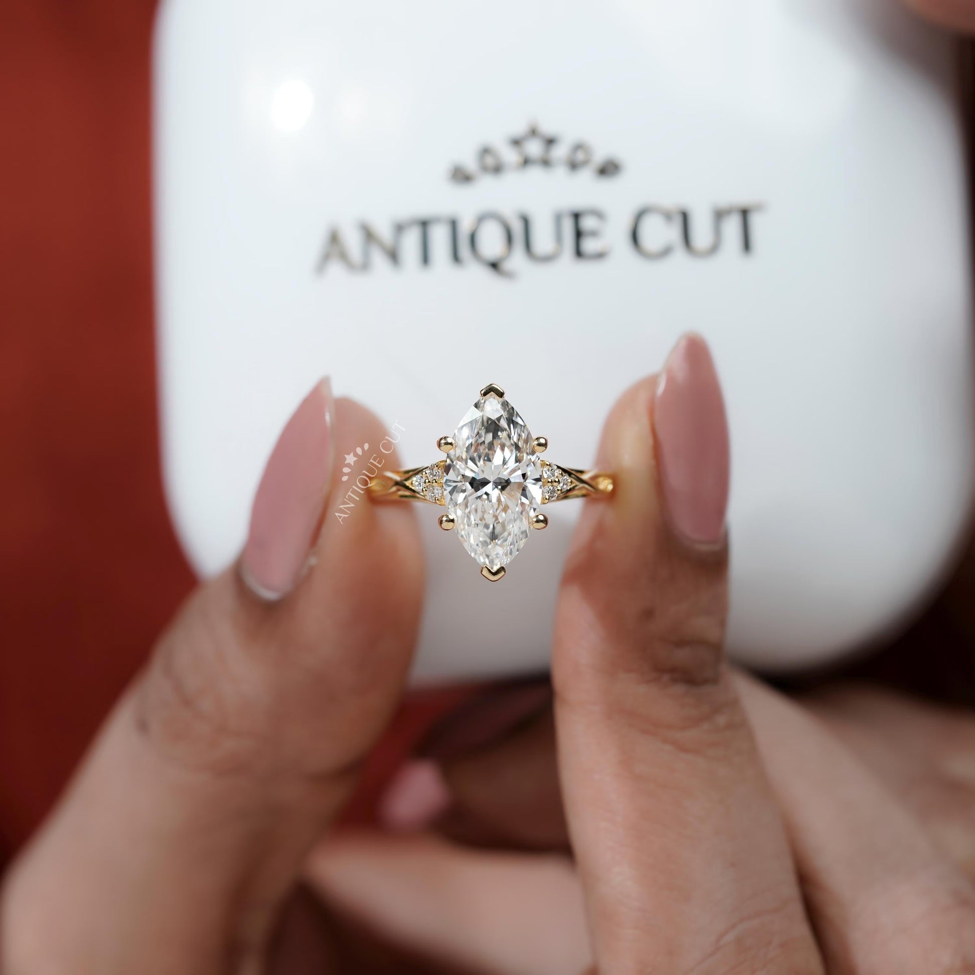 Gold diamond ring held by a hand with 'Antique Cut' jewelry box in the background