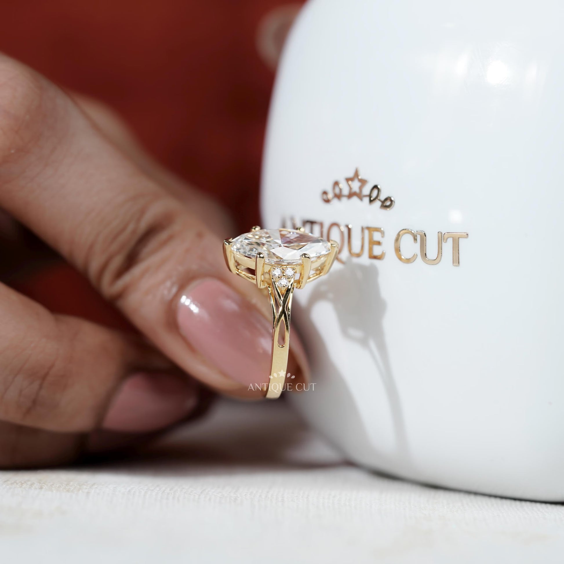 Gold ring with a diamond held against a white mug with 'Antique Cut' branding.


