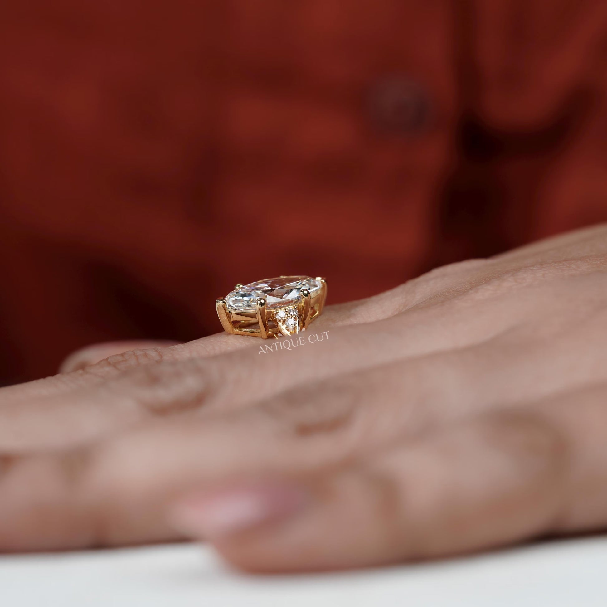 Gold ring with diamonds on a person's finger against a blurred red background

