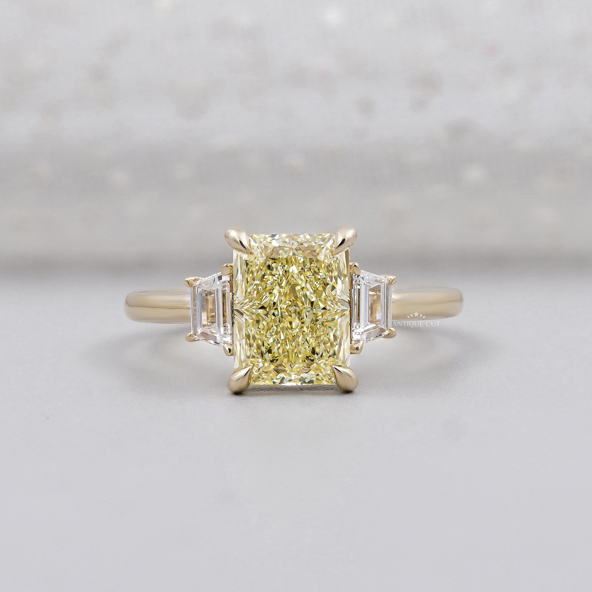 Radiant fancy yellow diamond ring in yellow gold with trapezoid side stones