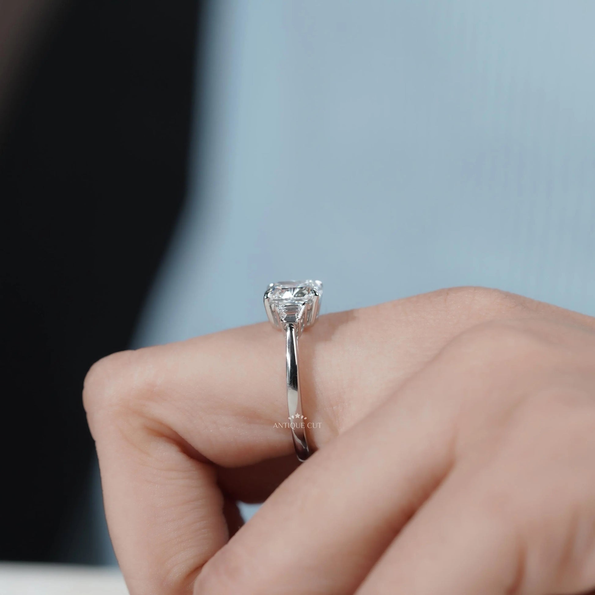 Cushion cut engagement ring with three-stone layout and tapered baguette side stones.