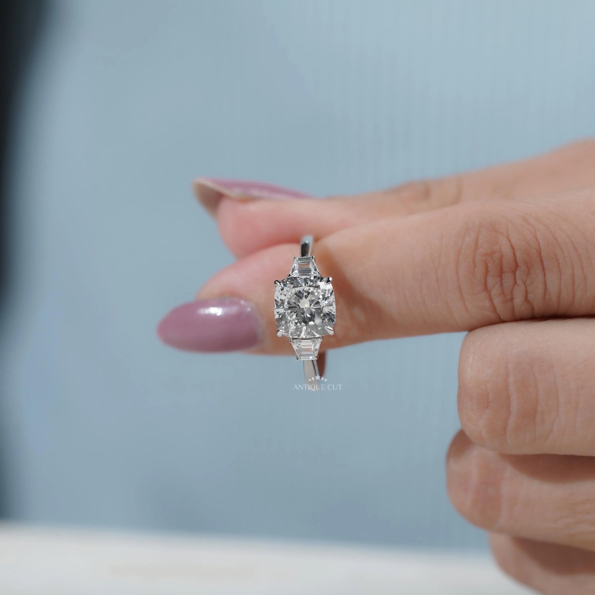 Side view of three-stone engagement ring with cushion cut diamond and baguette accents.