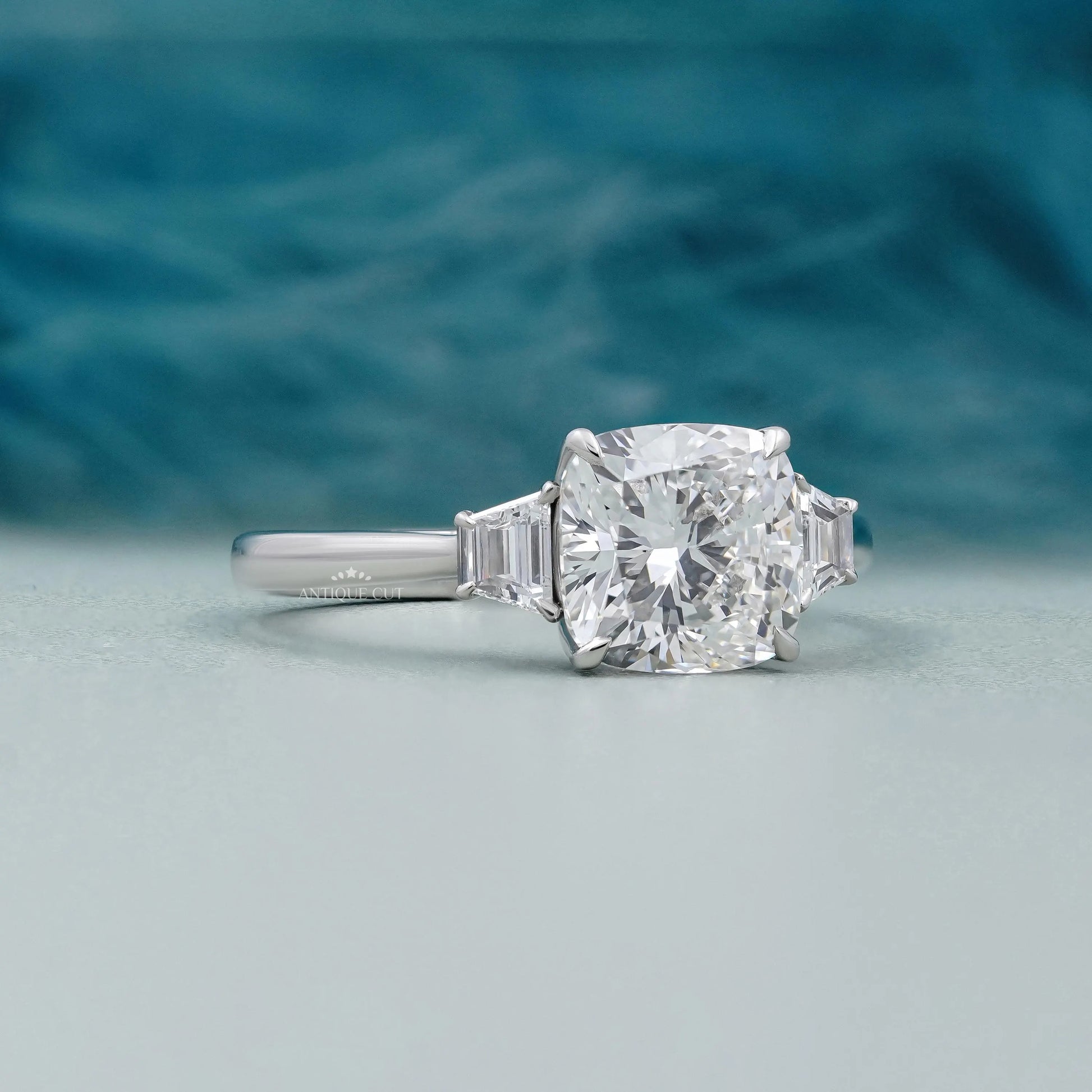 Elegant three-stone engagement ring featuring a cushion cut center and baguette side stones.