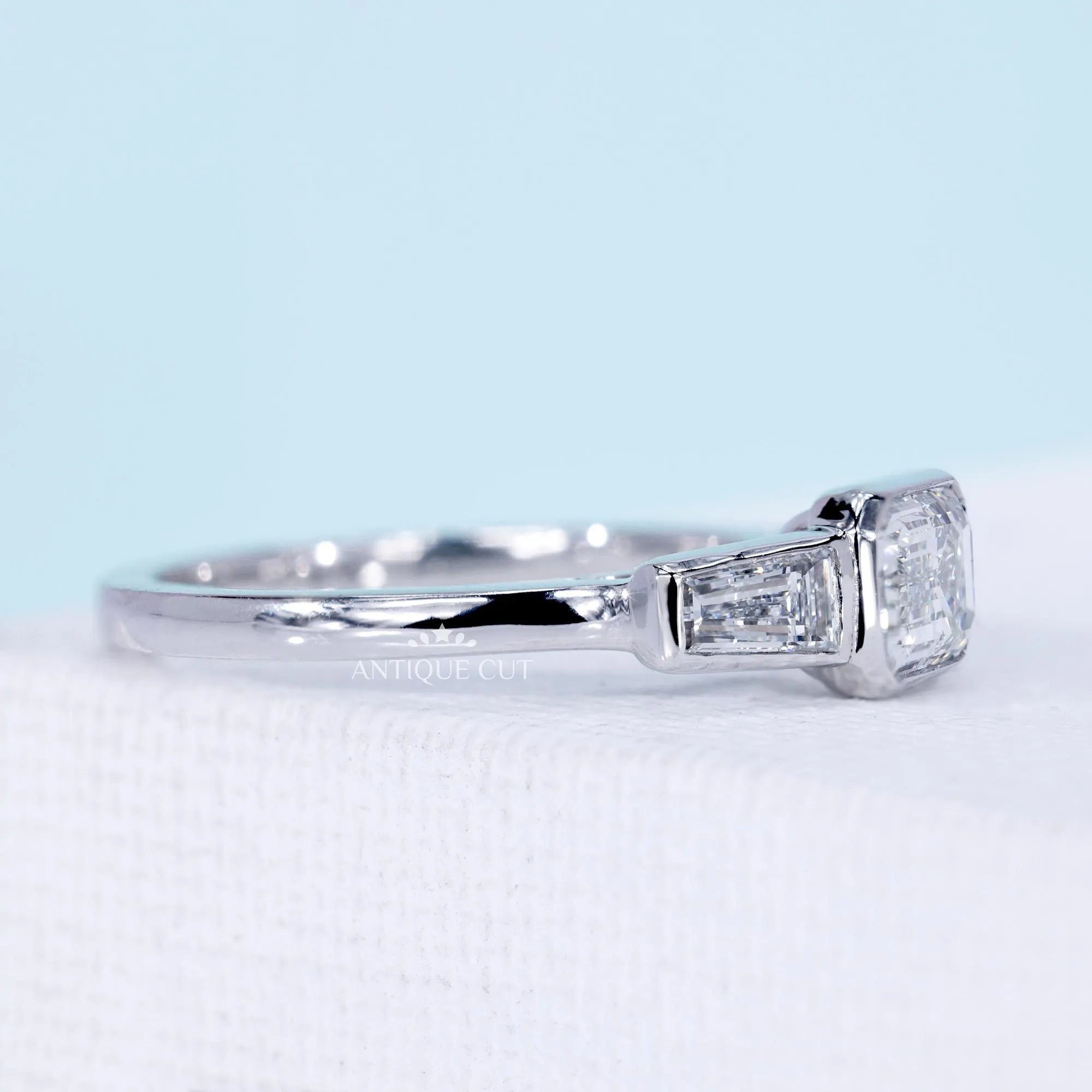Emerald cut east west engagement ring with three stone diamond design
