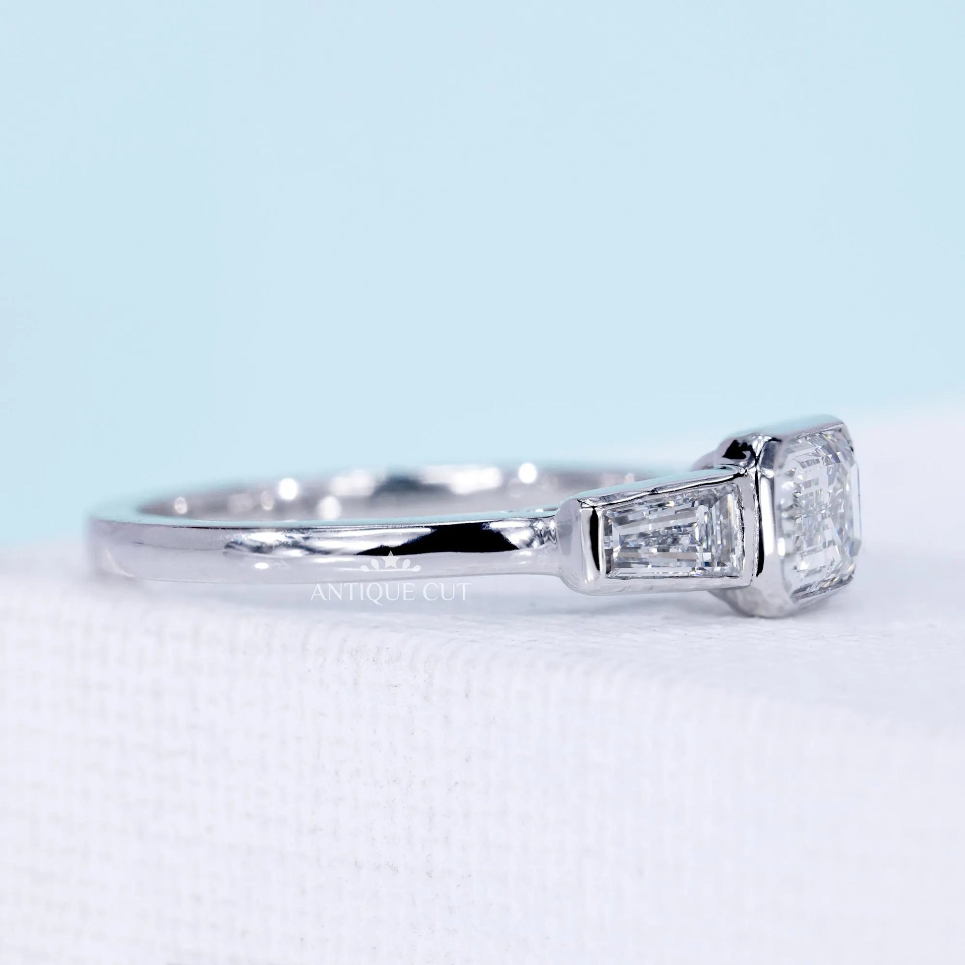 Emerald cut east west engagement ring with three stone diamond design
