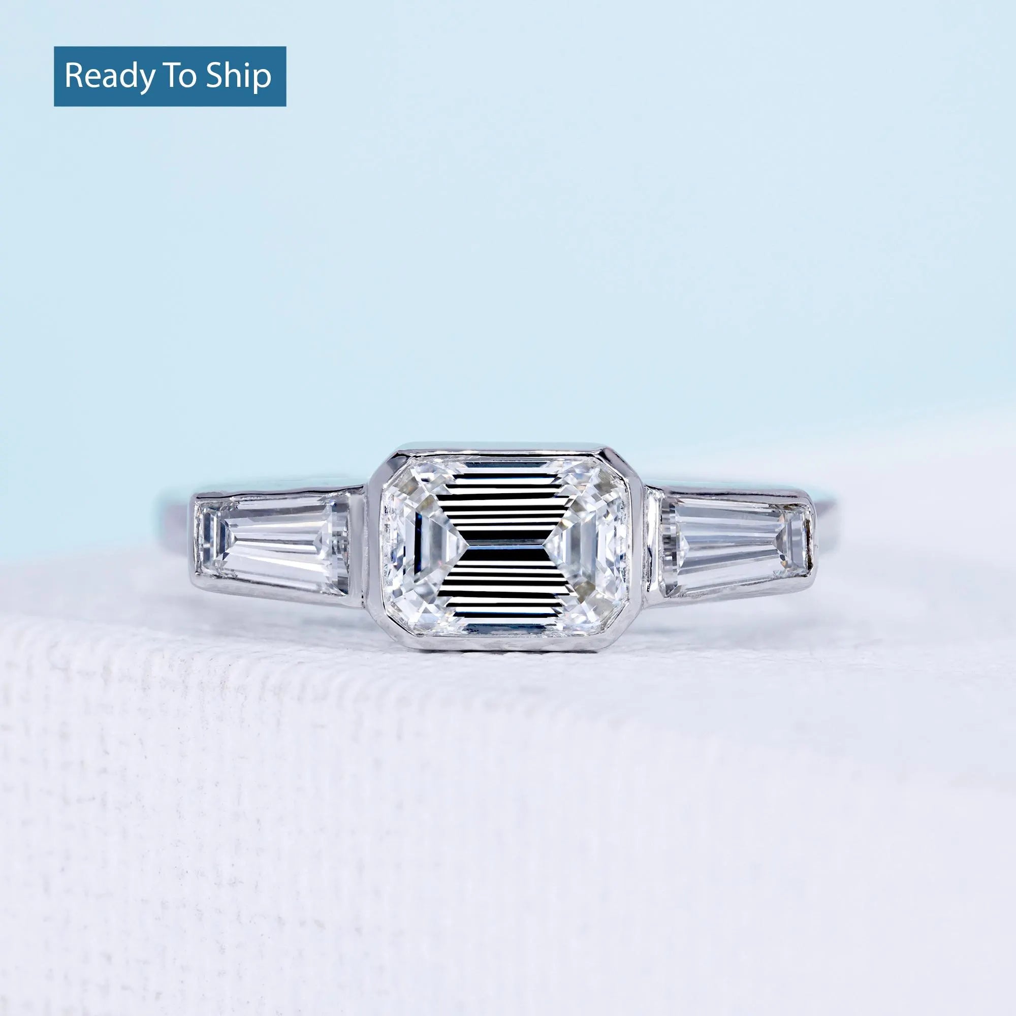 East west emerald cut ring with tapered baguette side stones and bezel setting

