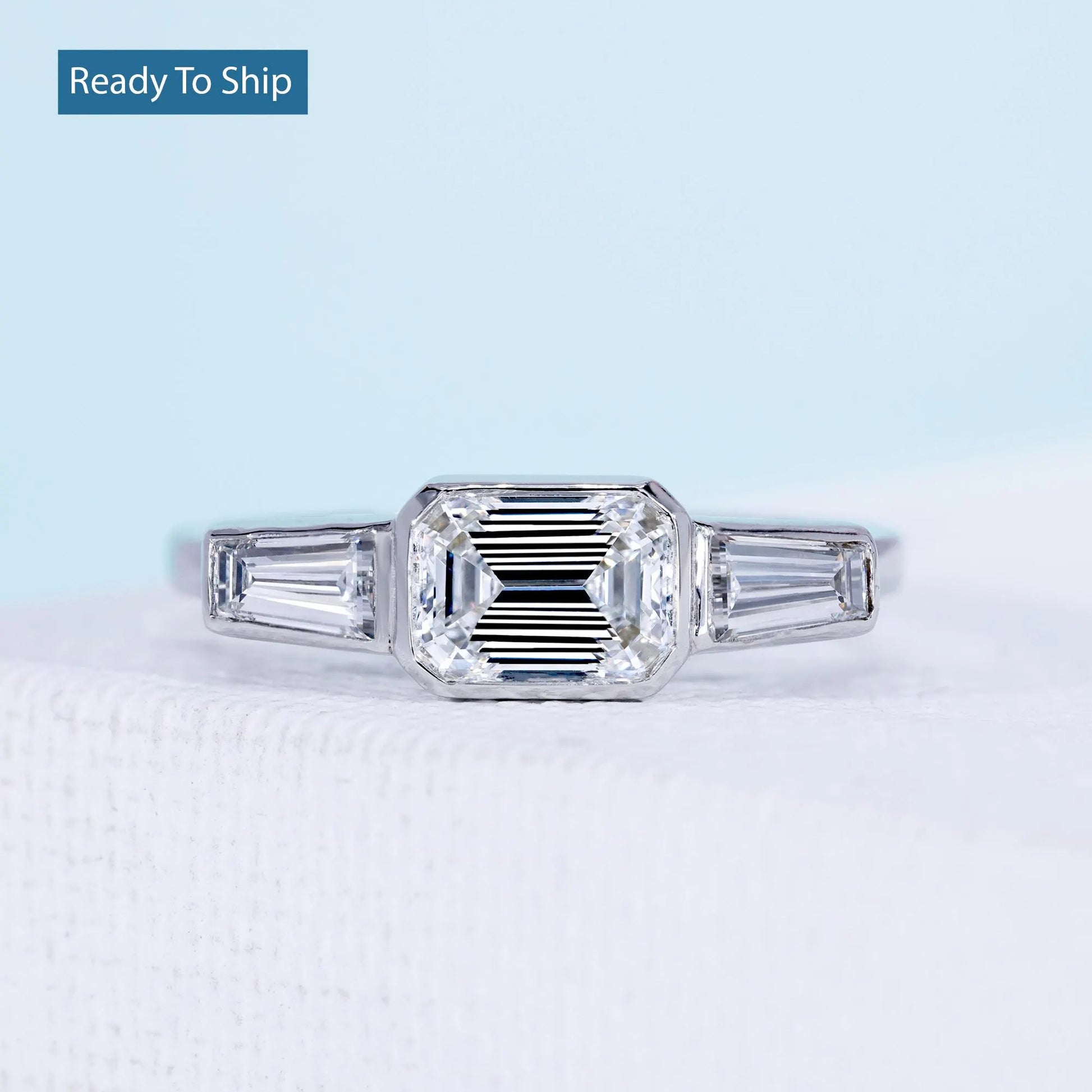 East west emerald cut ring with tapered baguette side stones and bezel setting
