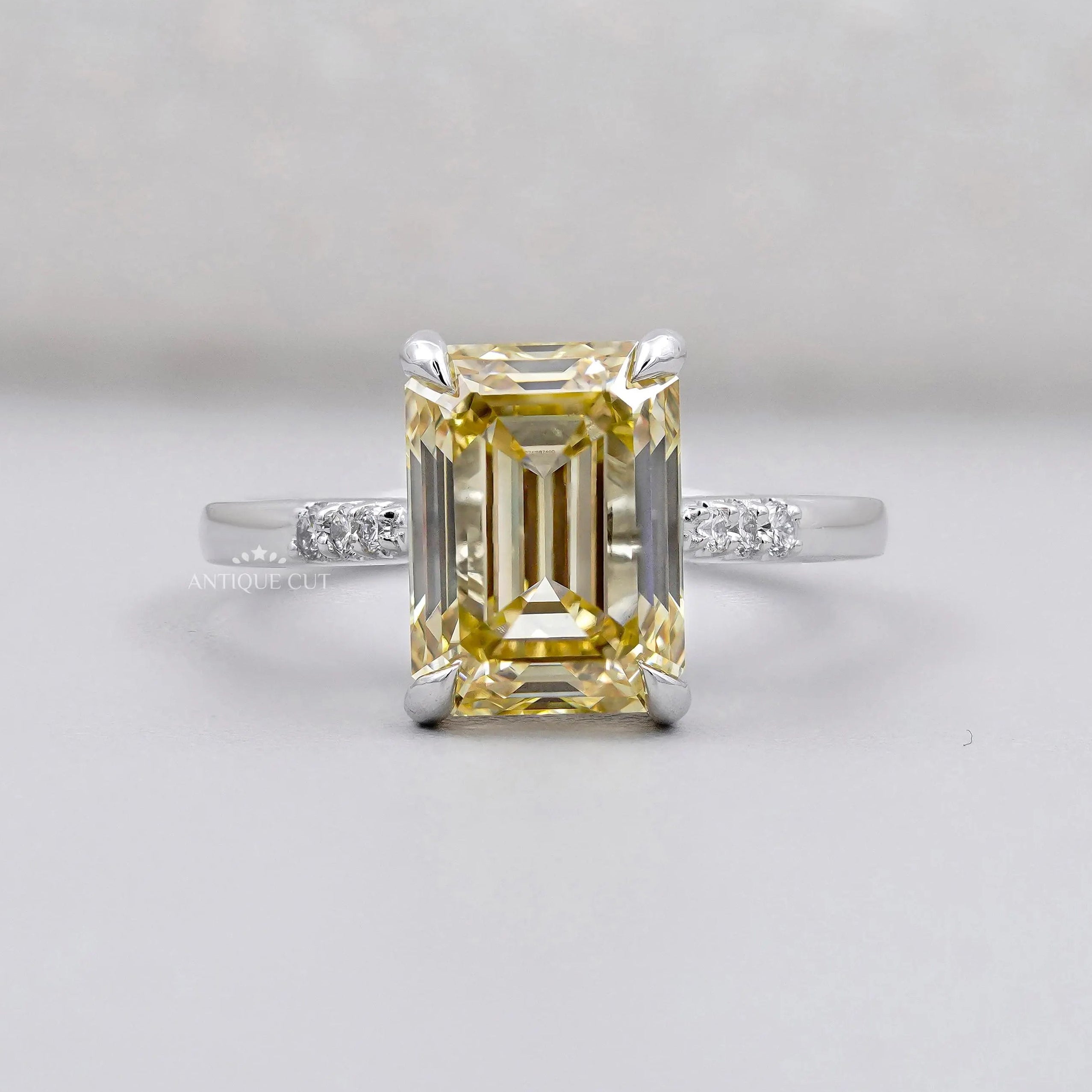 White gold ring with Yellow Emerald Cut Diamond and round side accents.