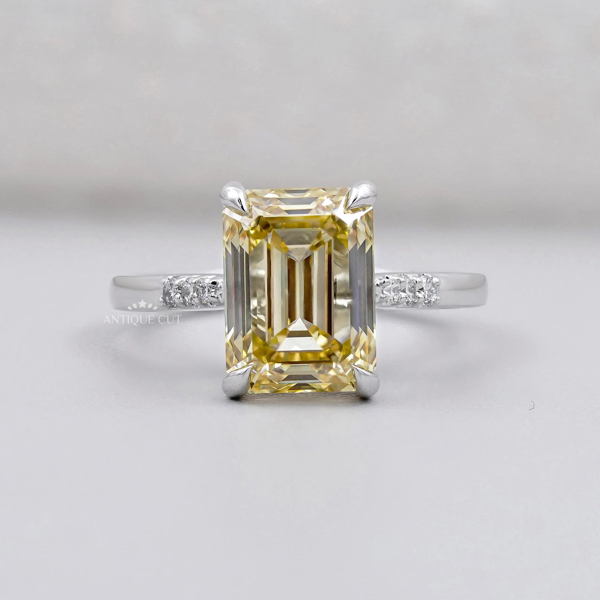 White gold ring with Yellow Emerald Cut Diamond and round side accents.