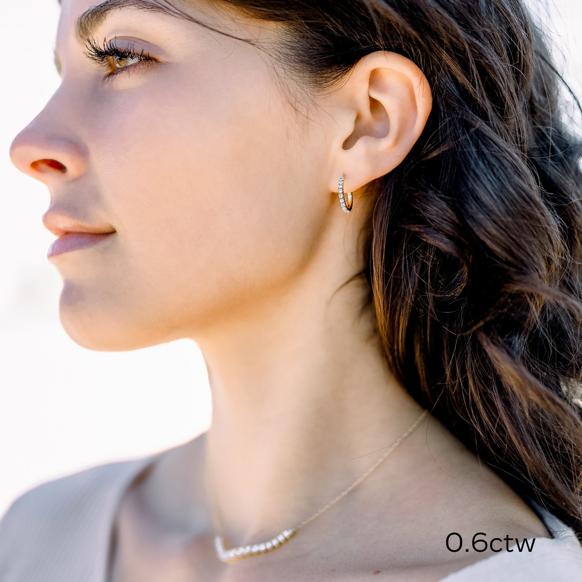 Woman wearing diamond hoop earrings and a necklace.
