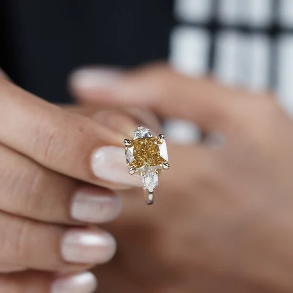 Fancy yellow cushion diamond ring featuring white trapezoid accent diamonds and four-prong design