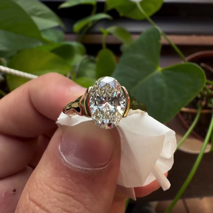 Wavy band oval diamond ring with half bezel setting.