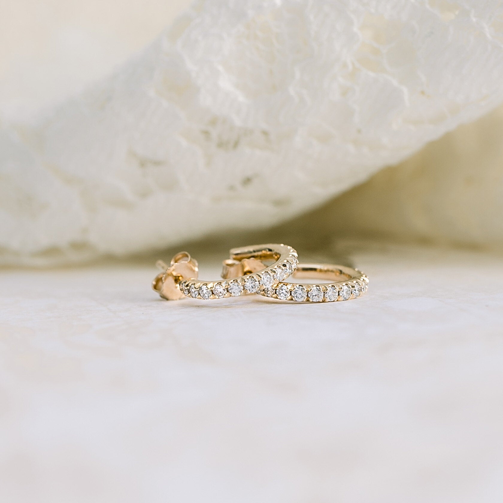 Gold and diamond hoop earrings on white lace.
